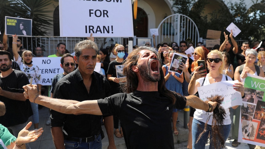 A man, holding his arms out as he holds his chopped off hair, screams at the sky during a protest.