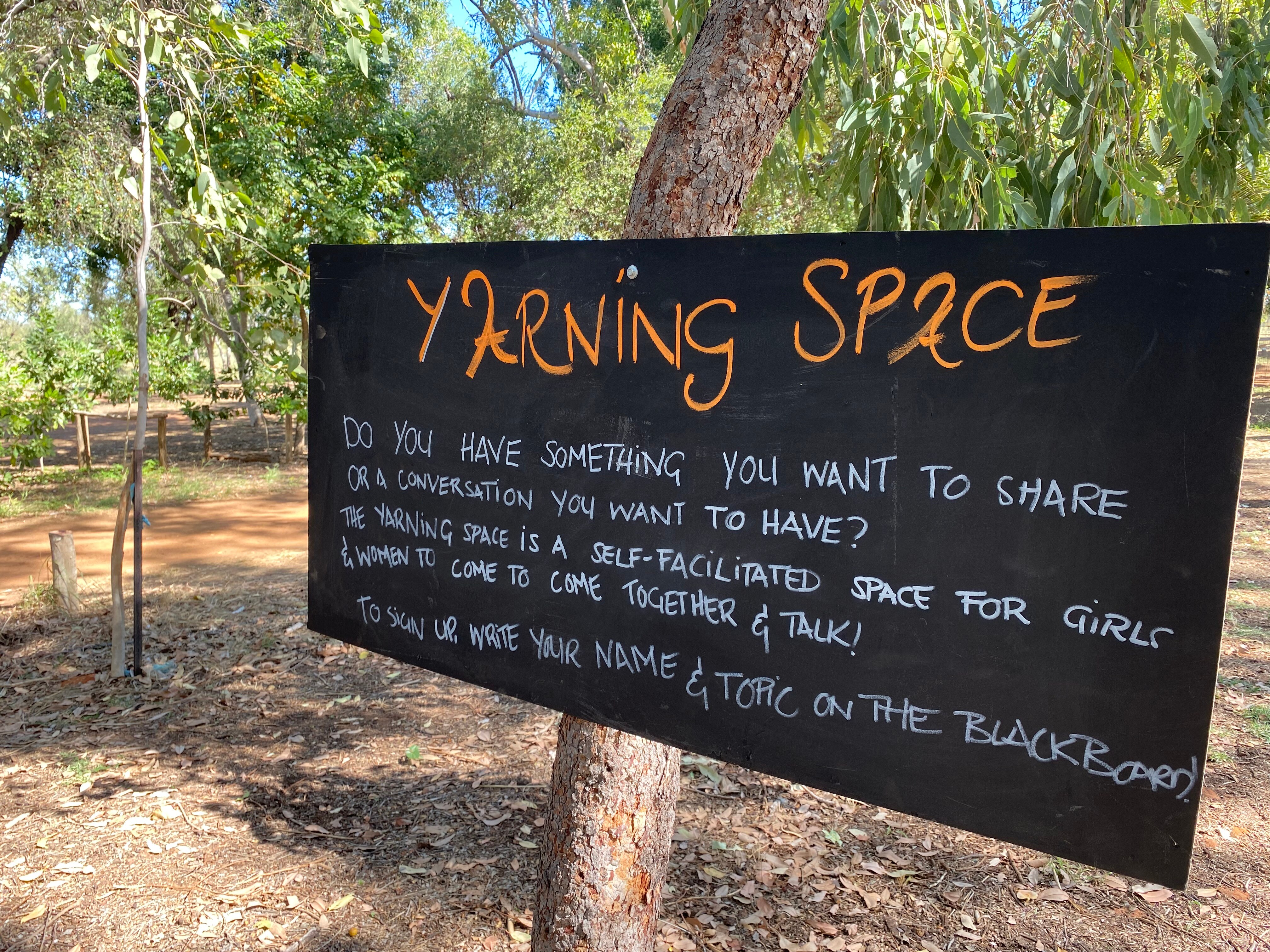 A black chalkboard sign with orange writing encouraging women to come and share their feelings