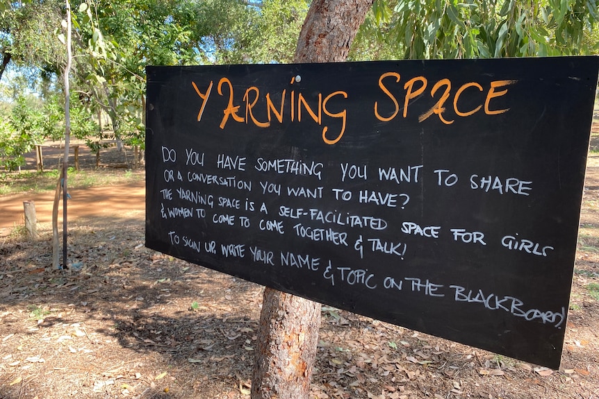 A black chalkboard sign with orange writing encouraging women to come and share their feelings