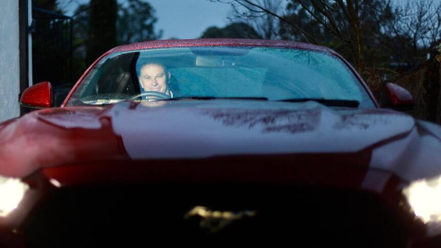 man sitting behind the wheel of his red mustang, looking out through the windscreen