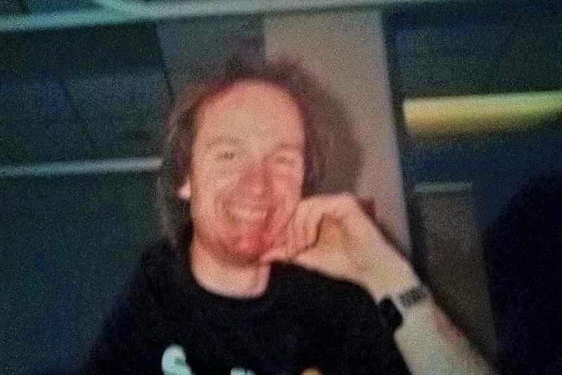 A photo of a man in a black shirt smiling with his hand leaned up against his chin 