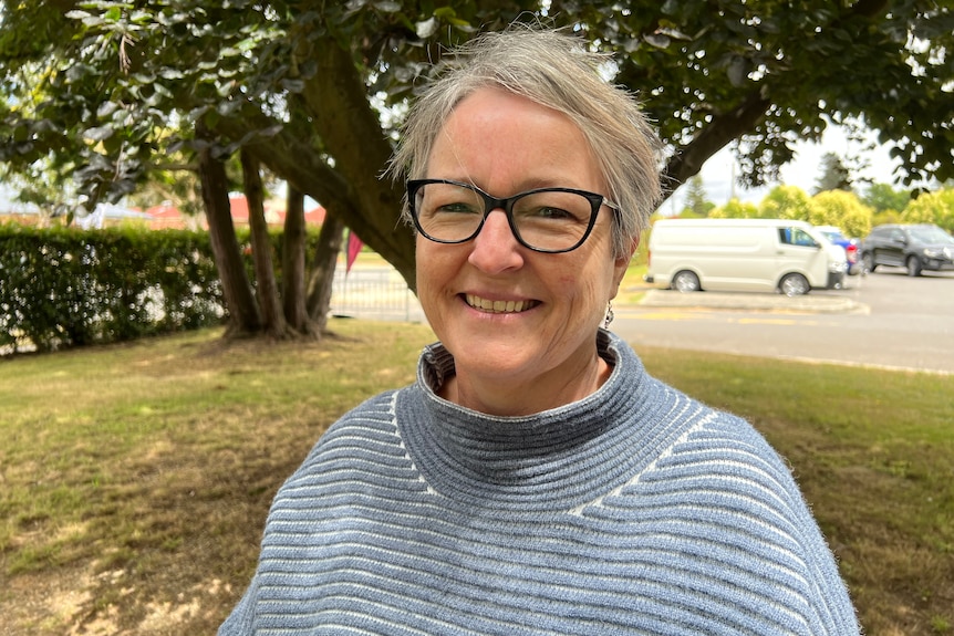 A woman with short hair and glasses smiles at the camera.