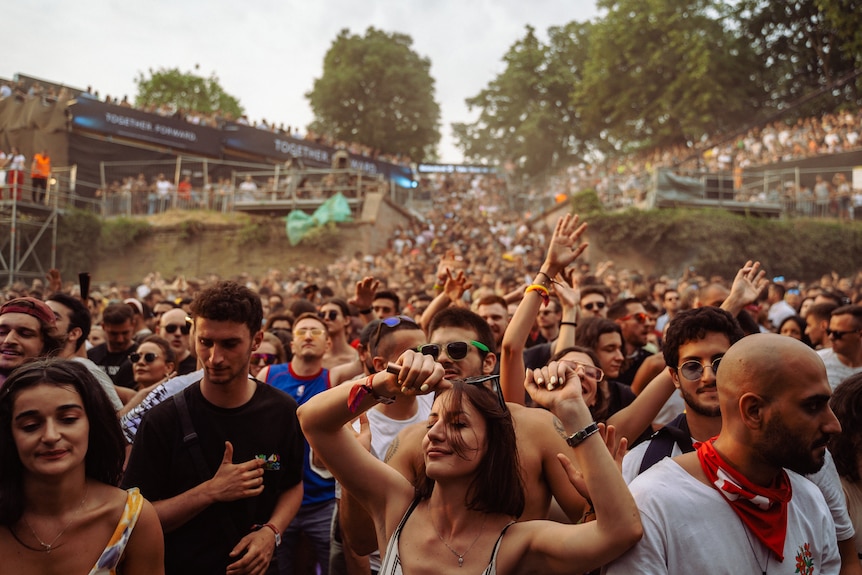 A crowd of people dance at a music festival, with the crowd sweeping back into the distance