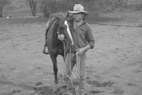 A black and white photo of an Indigenous man standing next to a horse.