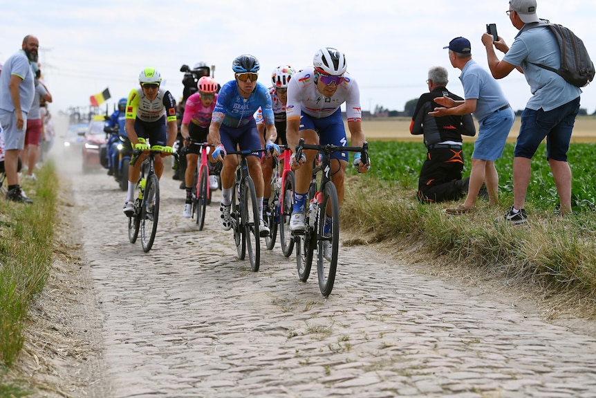 Simon Clarke is at the head of a pack of riders who are on a narrow cobblestone road