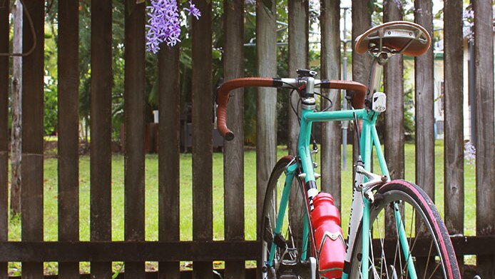 A turquoise bike against a wooden fence.