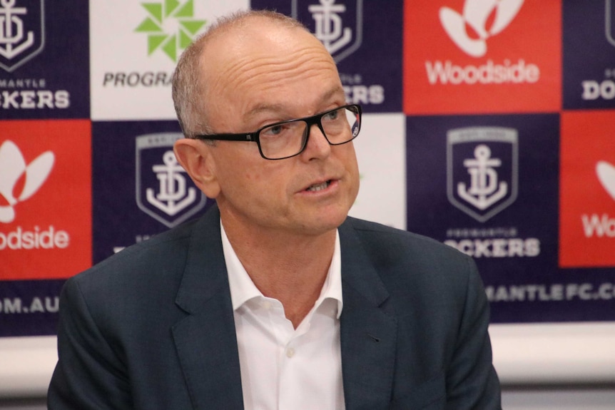 Dockers' chairman Dale Alcock speaks in front of a branded backdrop.