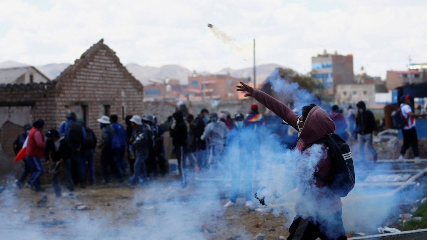 A man enveloped in tear gas, throws a cannister at a group of people
