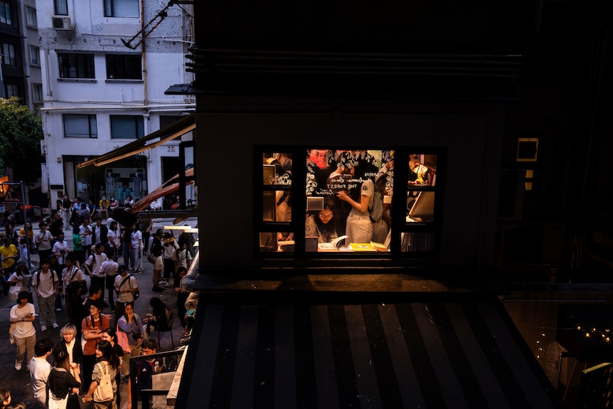 Visitors browse books as hundreds gather outside a closing bookshop at sunset.