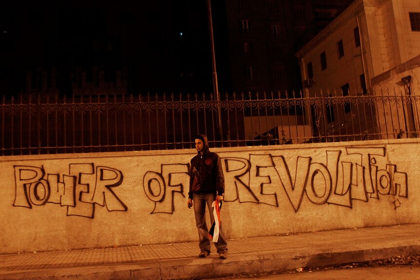 A young reveler stands in front of graffiti in Tahrir Square, Cairo