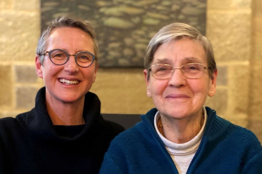 A middle-aged woman with glasses and her elderly mother, both smiling at the camera.