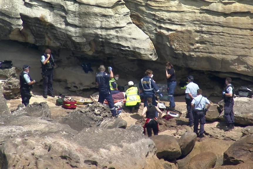 a group of people looking at a person getting treated by ambulance on a rock