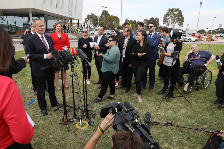 A man in a wheelchair listens on as Bill Shorten holds a press conference surrounded by journalists