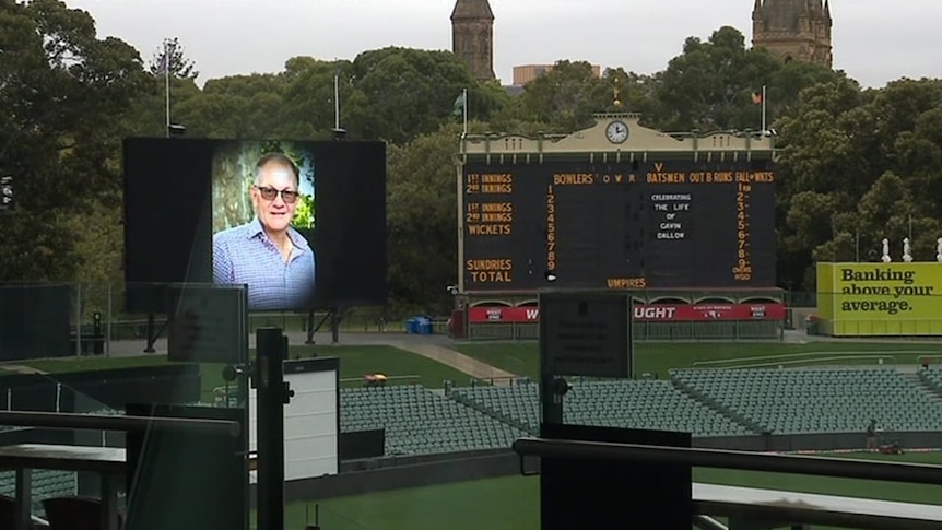 A man's picture on a big screen and words on an old scoreboard at a stadium