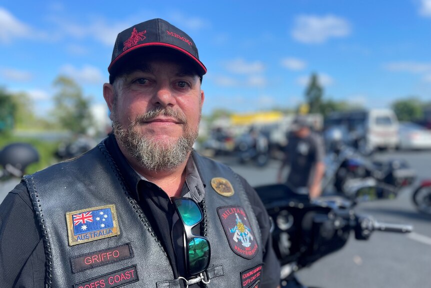 A portrait of a middle aged man wearing a cap and black motorbike jacket.