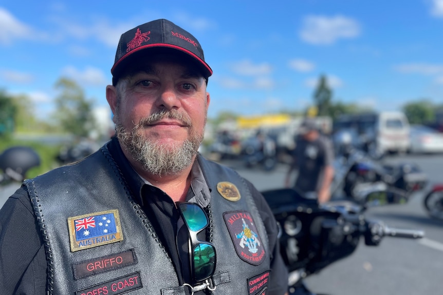 A portrait of a middle aged man wearing a cap and black motorbike jacket.