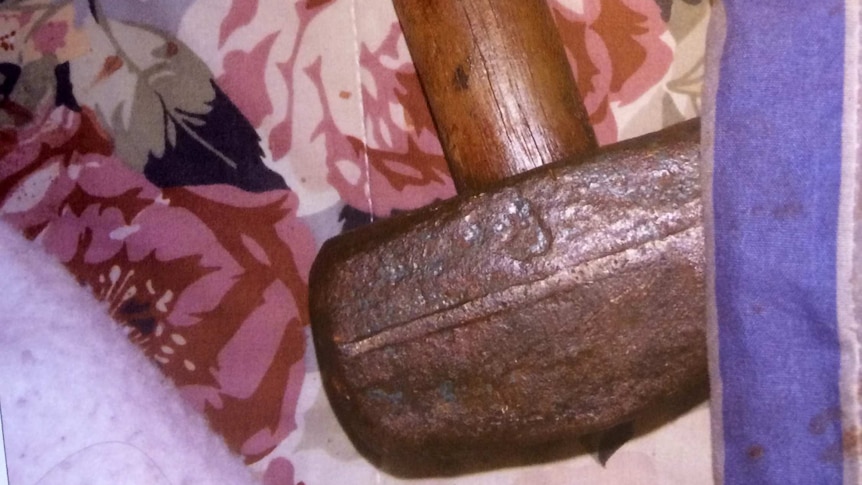 Close-up of metal-headed mallet with wooden handle next to bloodied bed linen.