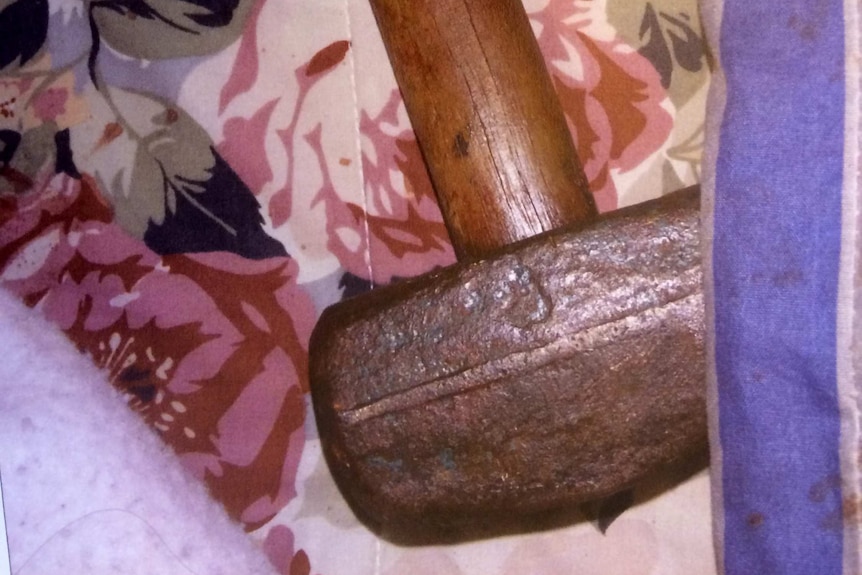 Close-up of metal-headed mallet with wooden handle next to bloodied bed linen.