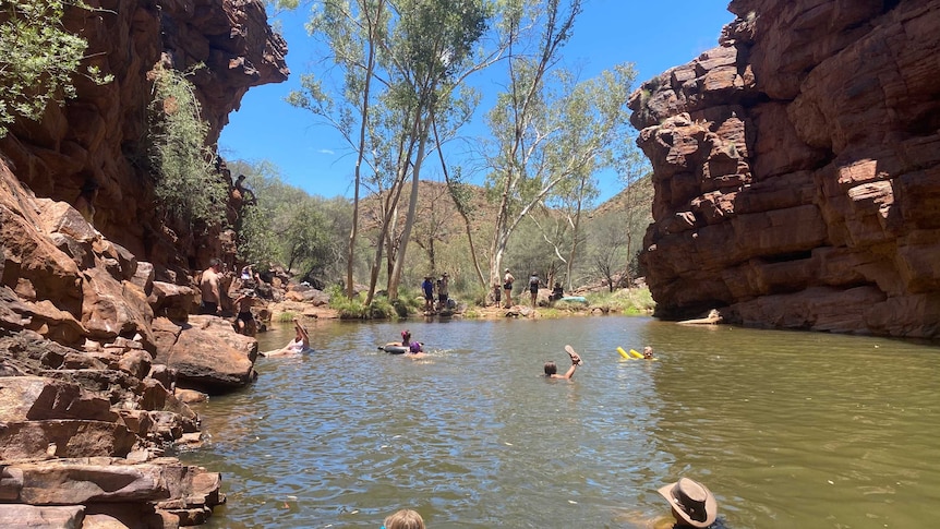 Waterhole in the middle of two cliffs with people swimming on flotation devices