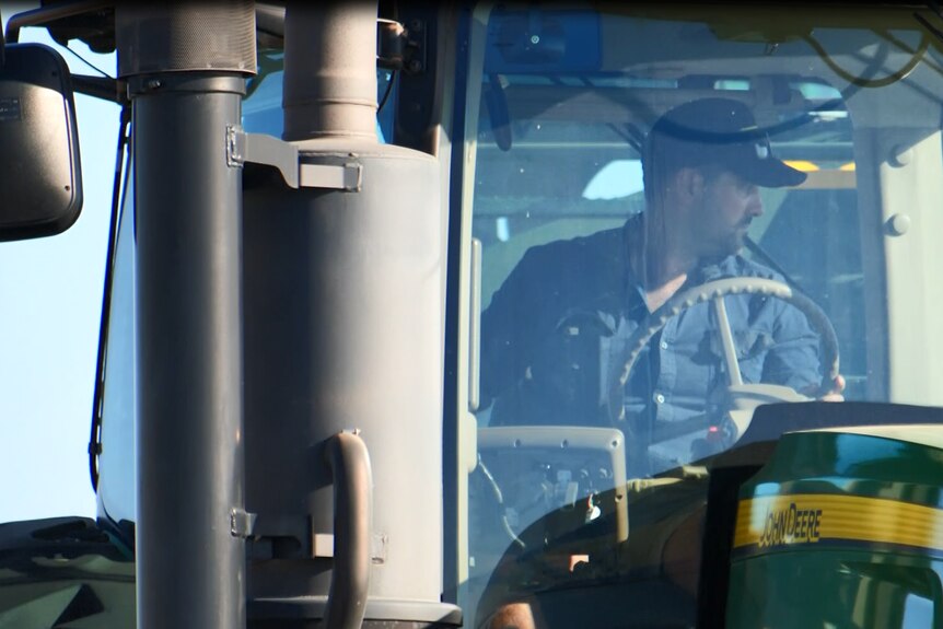A man wearing a cap sits in the cabin of a tractor