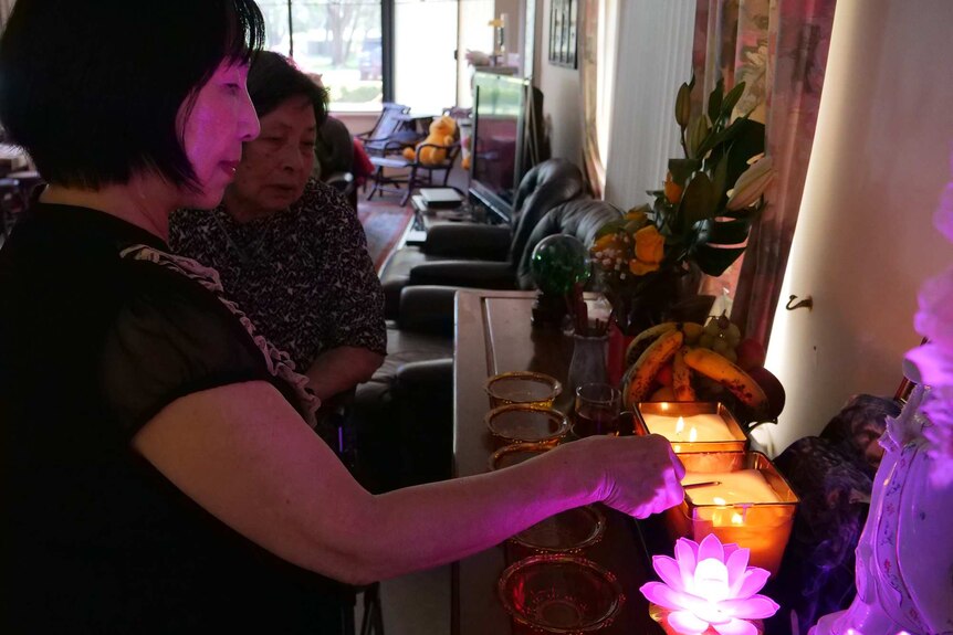 Two women light candles in front of a shrine.