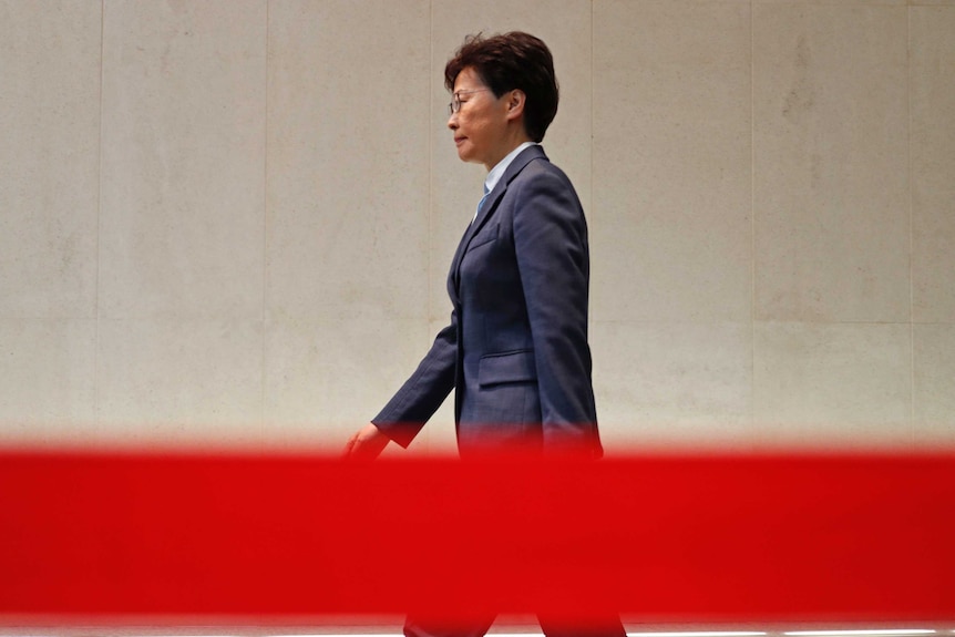 You see Hong Kong's Chief Executive Carrie Lam strut in a pant-suit behind a red tape.