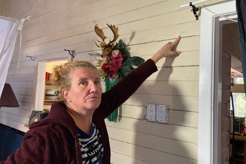 A woman points to a 2022 flood mark on her wall.