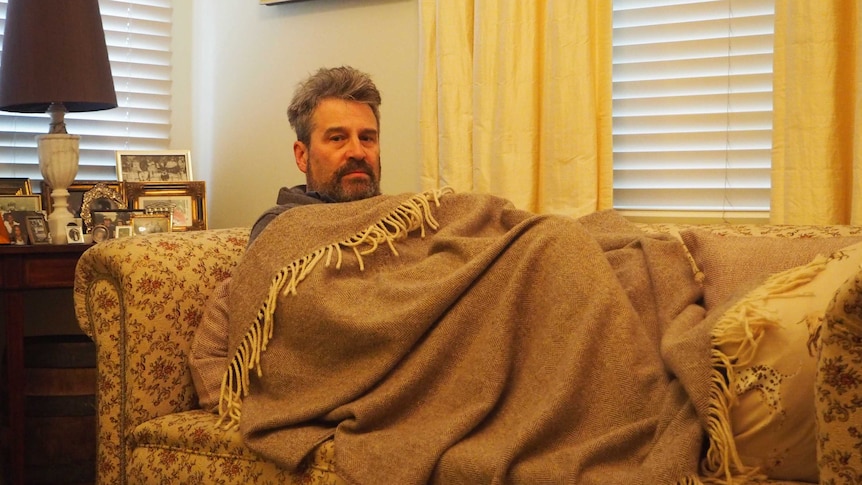 A sick man curled up in a blanked on a couch