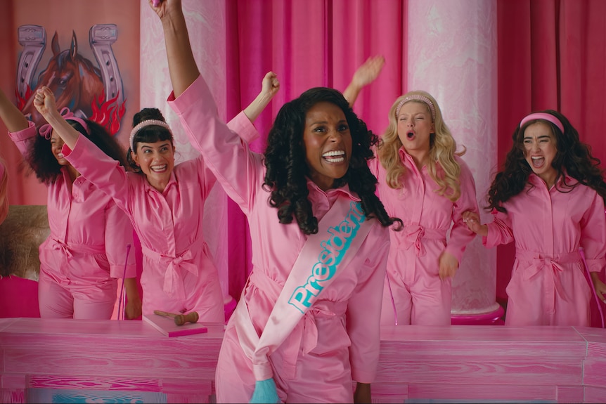 Issa Rae wearing pink and a sash saying President with hand in air, women behind her in pink also with hands in air