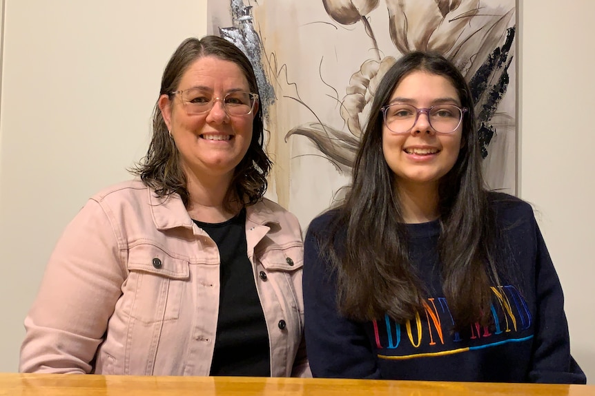 two women are sitting at the table both wearing glasses smiling at the camera 