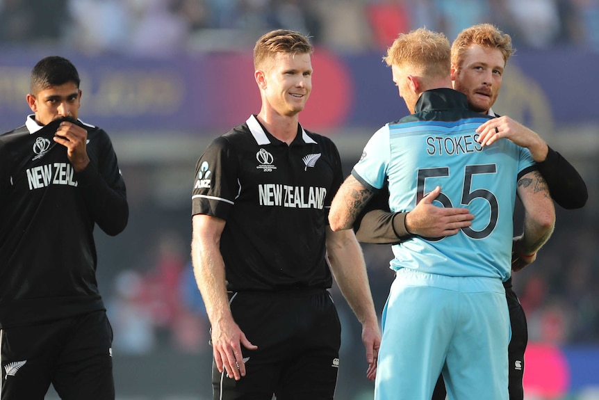 Two cricket players hug to congratulate each other as other players look on.