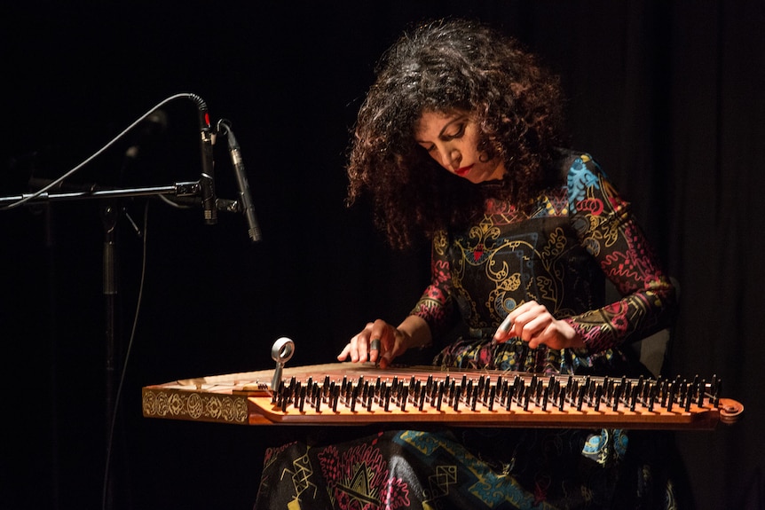 Maya Youssef performs on stage sitting with a qanun across her lap as she plucks the strings.