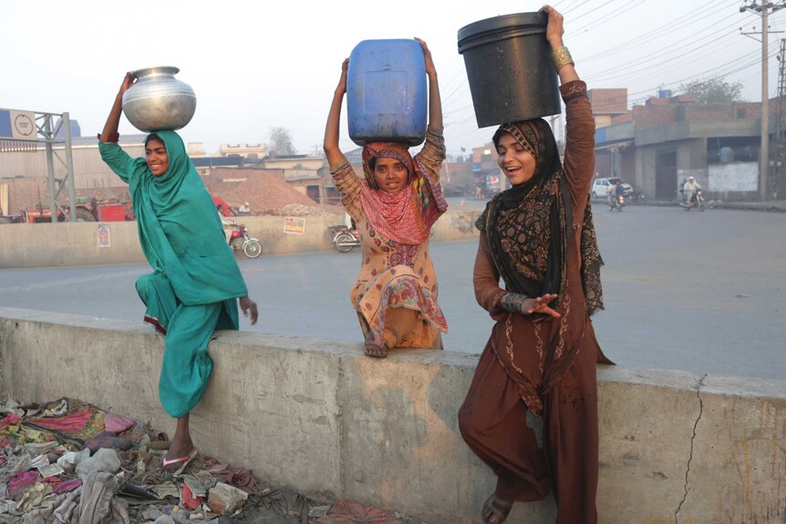 Pakistani girls living in Lahore's slums carry clean water in jugs on their heads