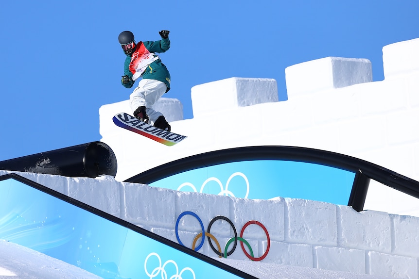 An Australian snowboarder turns in mid-air, above a column of ice during a run in the snowboard slopestyle.