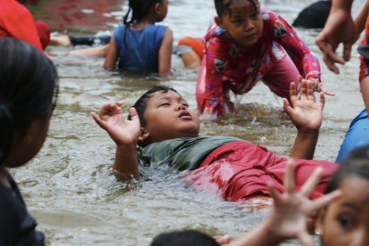 Indonesian children splash around and swim in ankle-deep flood waters.
