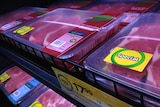Packaged beef stacked on a refrigerated supermarket shelf.