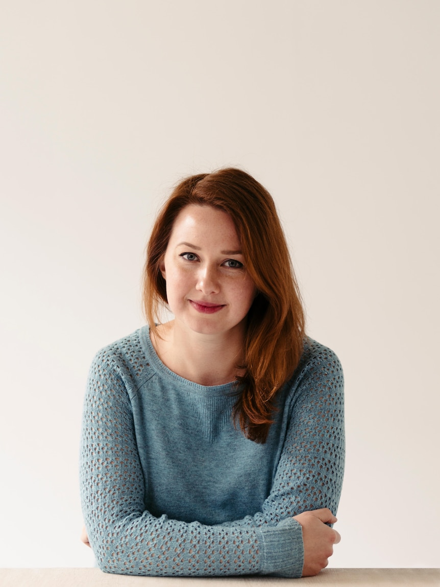 A woman in her late 30s with red hair and a small smile, staring at the camera