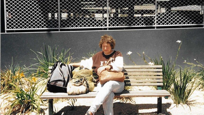 A photo from the 1980s or 1990s shows a woman sitting on a bench outside a supermarket, looking sad.
