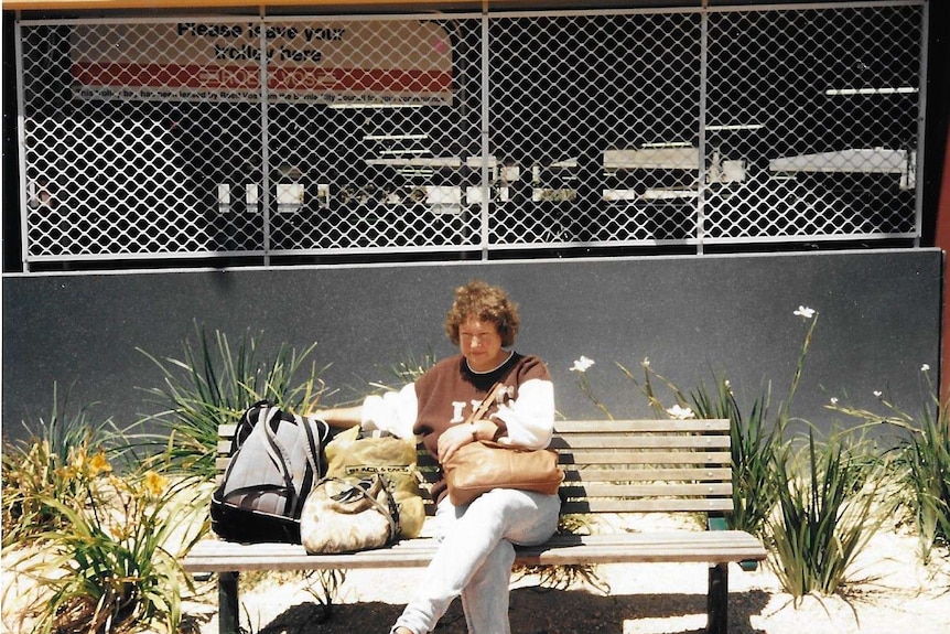 A photo from the 1980s or 1990s shows a woman sitting on a bench outside a supermarket, looking sad.