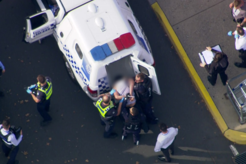 Police officers put a person into the back of a divisional van, viewed from helicopter footage.