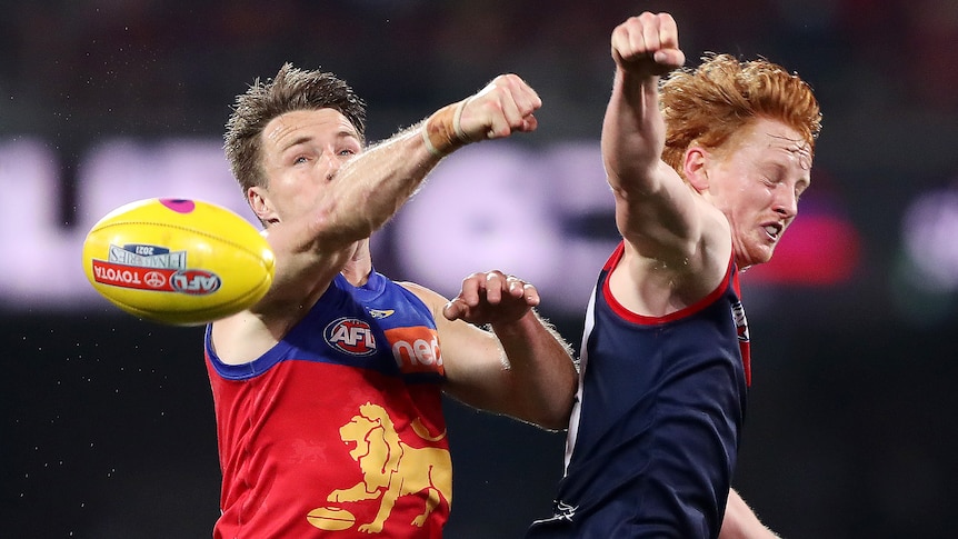 A Brisbane Lions AFL player contests for the ball alongside a Melbourne opponent.