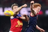 A Brisbane Lions AFL player contests for the ball alongside a Melbourne opponent.