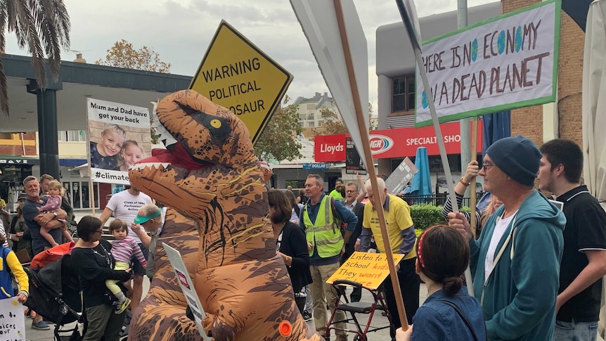 a large brown blow-up dinosaur front of picture surrounded by people and posters