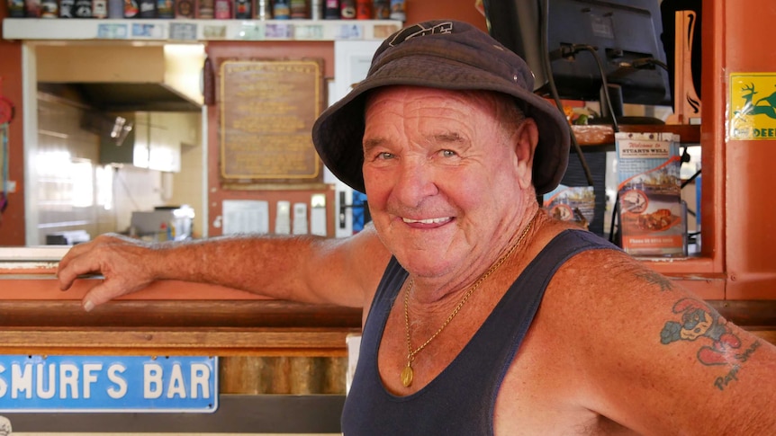 Peter 'Spud' Murphy is at a bar smiling at the camera. He's wearing a hat and a singlet.