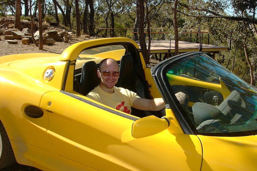 Mike Smith sits in the driver's seat of a yellow sports car with its roof down