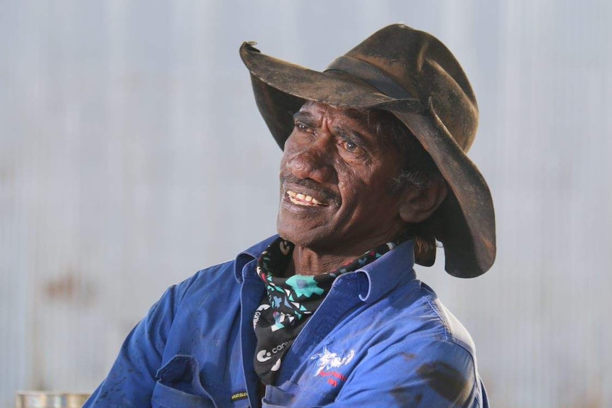 He wears a battered hat, a blue work shirt and a handkerchief around his neck