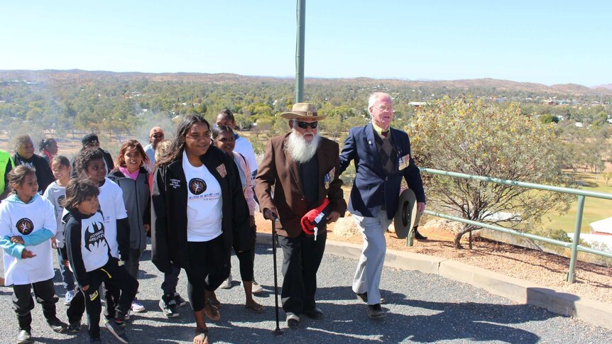 Geoffrey Shaw is flanked by children and a friend as he walks up Anzac Hill