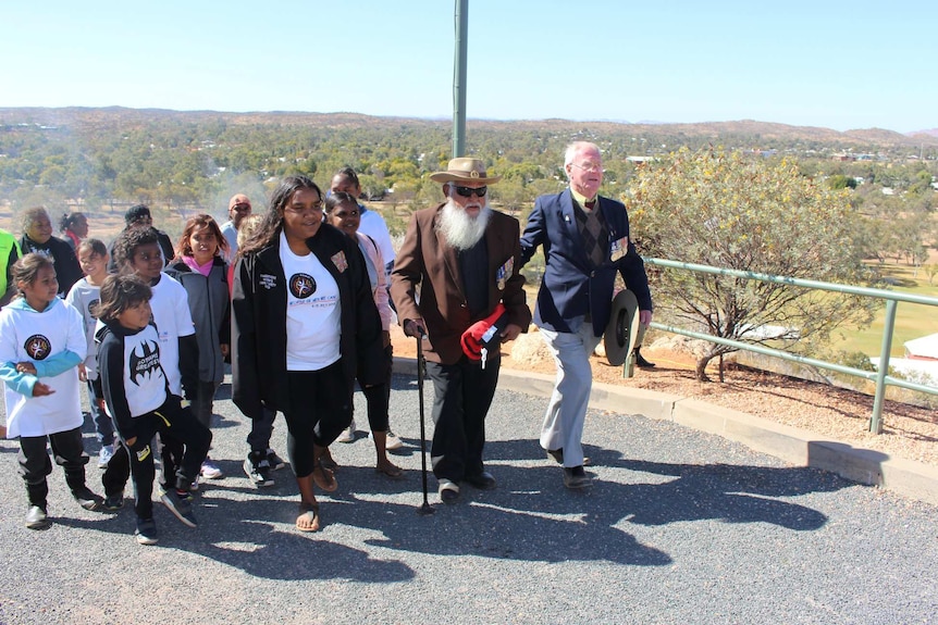 Geoffrey Shaw is flanked by children and a friend as he walks up Anzac Hill