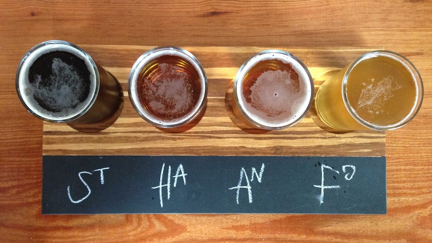 A set of four different beers on a tasting paddle, on a wooden table.