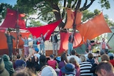 A group of people on an outdoor stage adorned with ship sails take a bow.